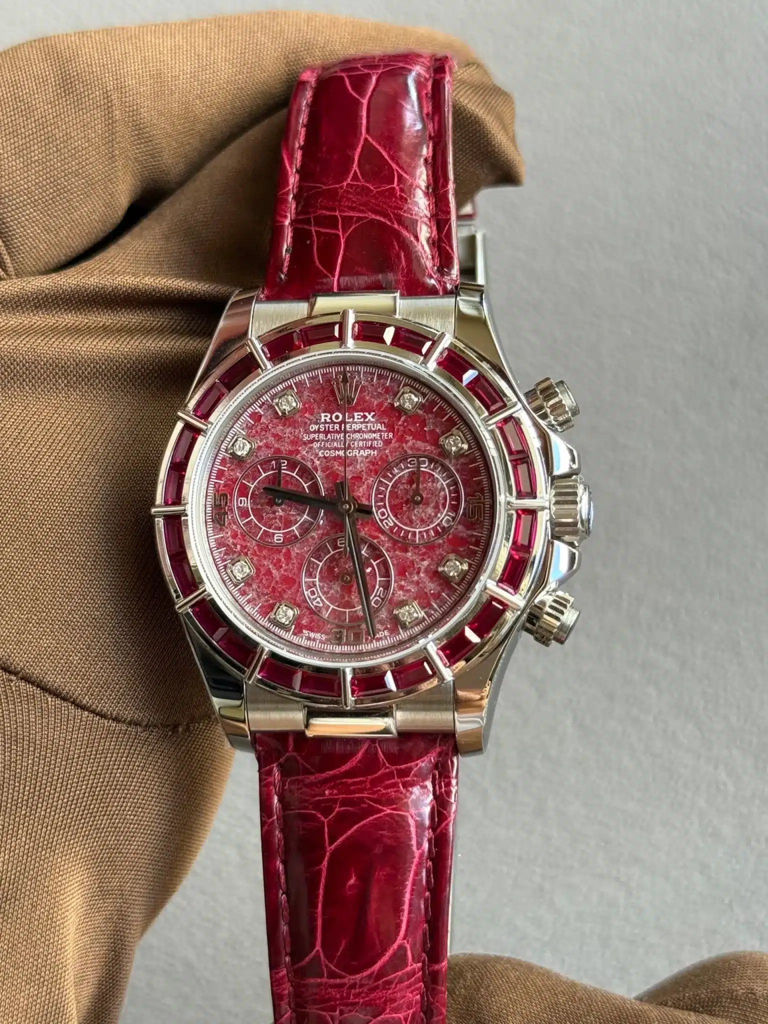 Rolex chronograph with red textured dial, diamond hour markers, ruby-red bezel, and red leather strap.