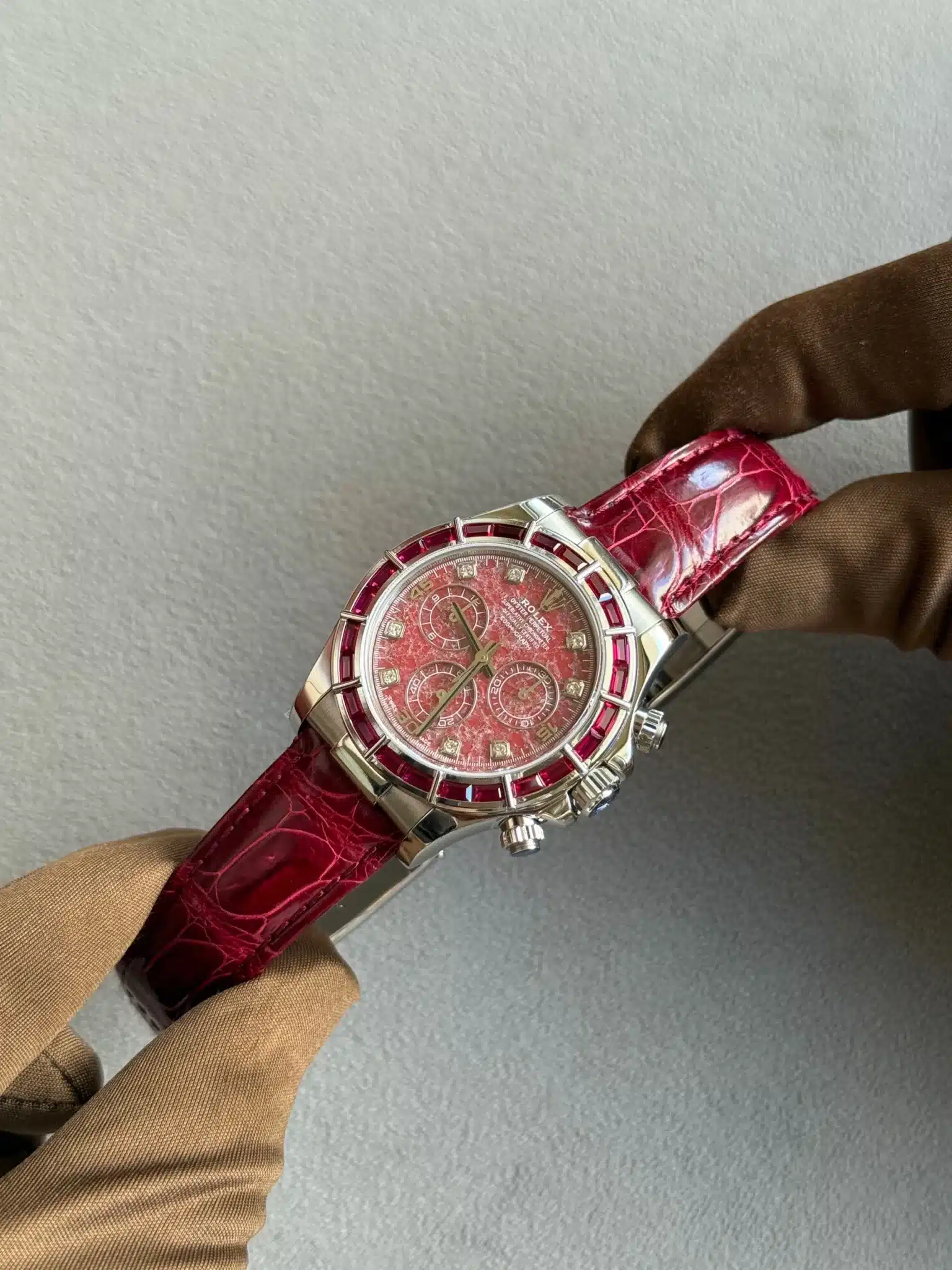 Luxurious wristwatch with red dial, ruby bezel, and red leather strap held by gloved hands.