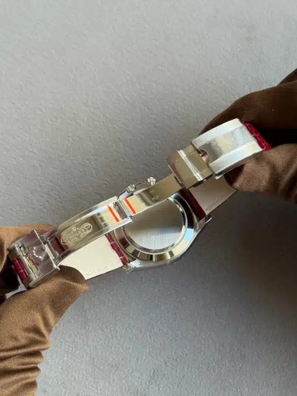 Close-up of a stainless steel Rolex watch held by gloved hands, showing the open deployant clasp and the brushed case back with a white inner strap.