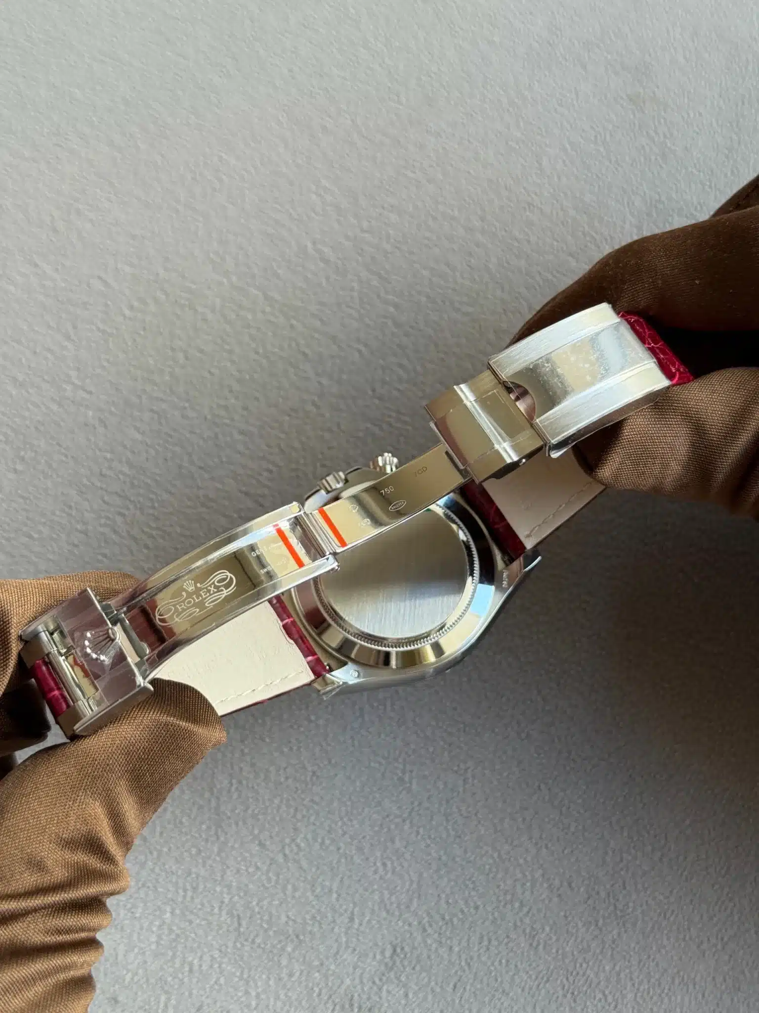 Close-up of a stainless steel Rolex watch held by gloved hands, showing the open deployant clasp and the brushed case back with a white inner strap.