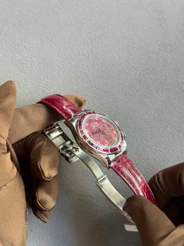 Luxurious women's wristwatch with a pink dial, red gemstone bezel, and pink crocodile-strap, held by gloved hands.