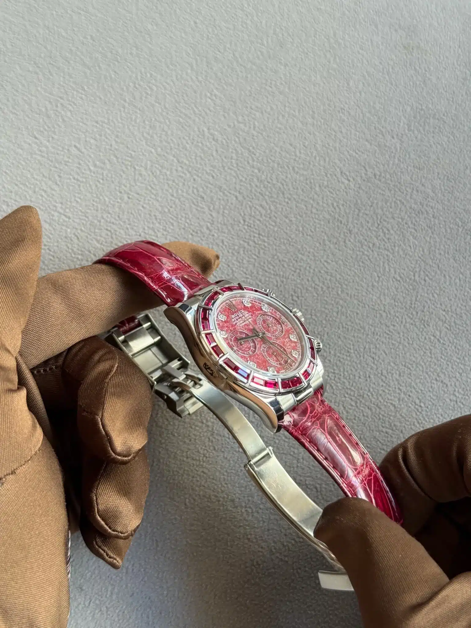 Luxurious women's wristwatch with a pink dial, red gemstone bezel, and pink crocodile-strap, held by gloved hands.