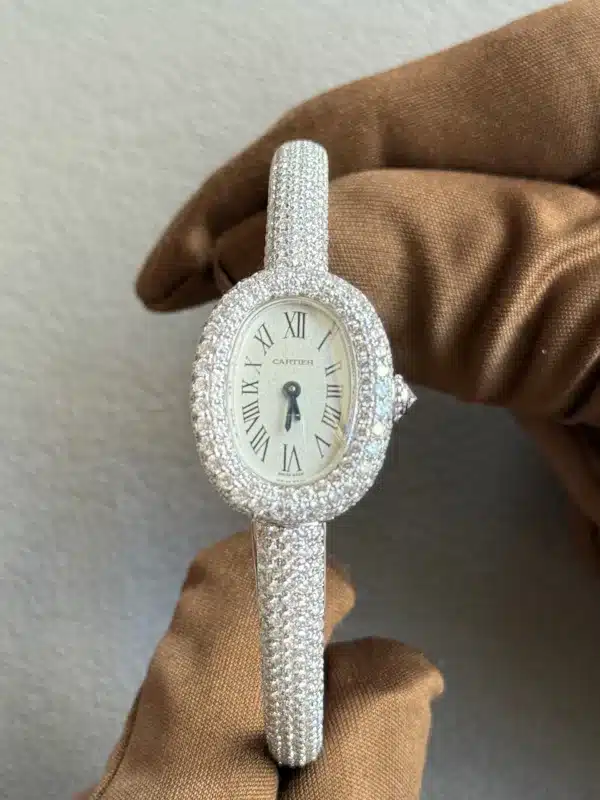 Diamond-encrusted Cartier watch with a Roman numeral dial held by a gloved hand.