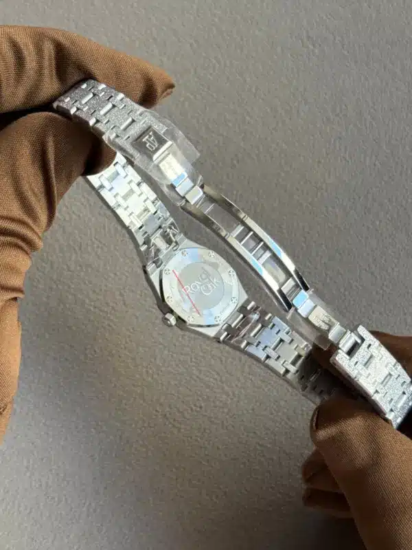 Stainless steel Rolex watch held by a gloved hand, showing the case back and bracelet links on a gray background.