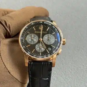 Gold Audemars Piguet chronograph watch with black dial and multiple subdials, held by a gloved hand.