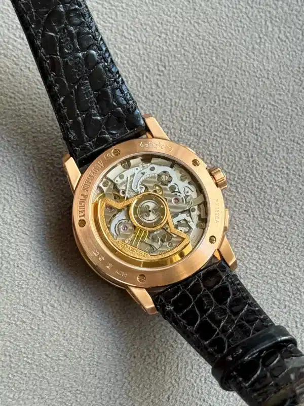 Gold-tone wristwatch with a see-through (skeleton) movement and a black textured leather strap on a gray fabric surface.