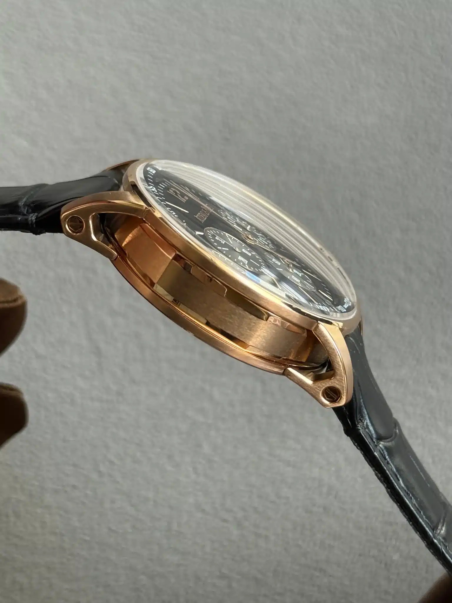 Gold-tone wristwatch with a black leather strap, shown in a side view highlighting the case and dial details.
