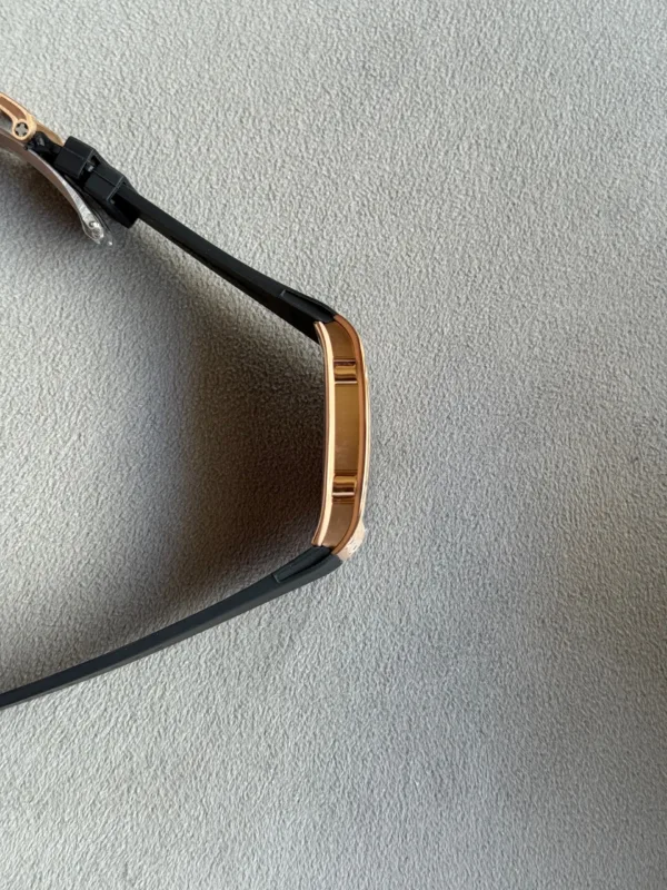 Partially visible wristwatch with a black band and rose-gold case on a gray textured surface.