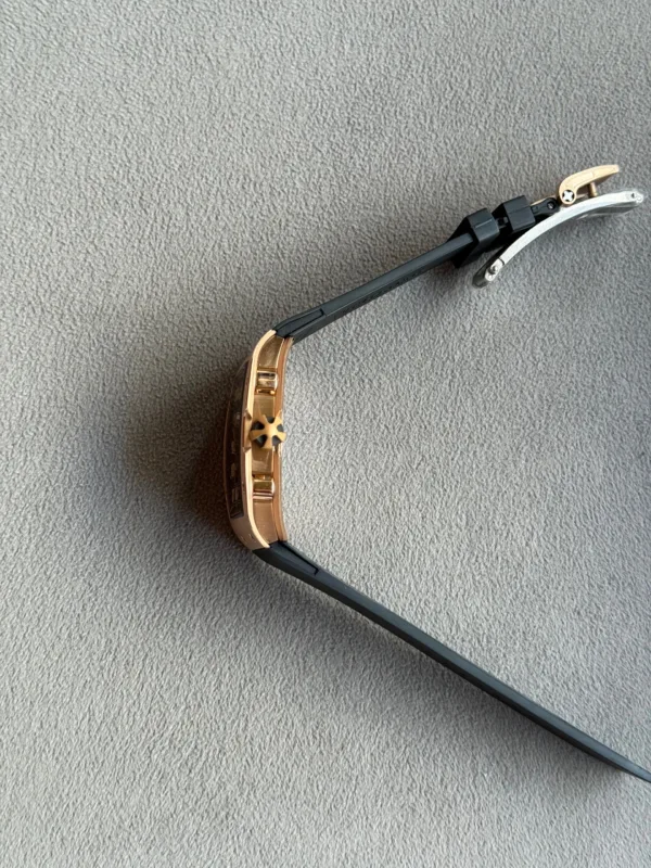 Close-up of a rose-gold wristwatch with a black strap and gold-tone clasp on a gray textured surface.