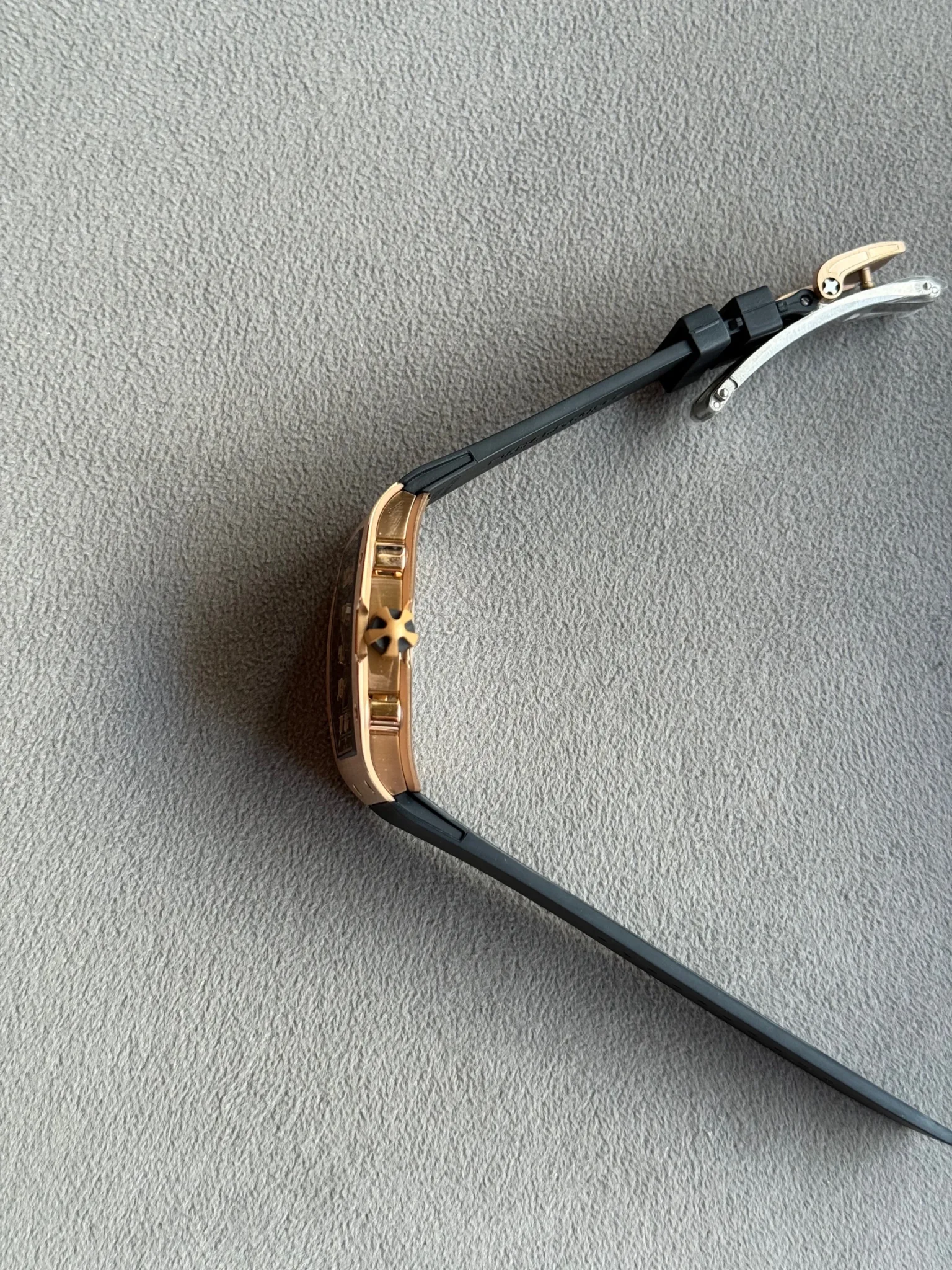 Close-up of a rose-gold wristwatch with a black strap and gold-tone clasp on a gray textured surface.