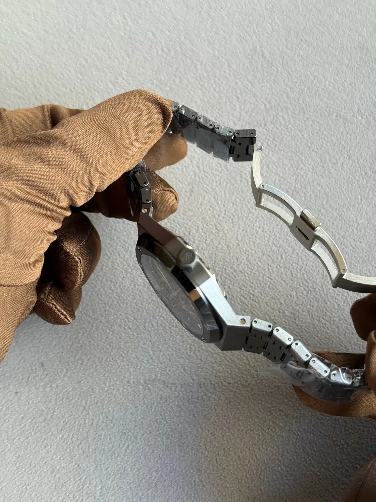 Close-up of a gloved hand using pliers to remove a link from a metal watch bracelet.