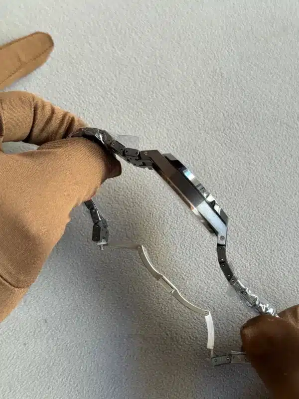 Close-up of a person in a brown sleeve manipulating a small black metal articulated robotic arm on a gray carpet.
