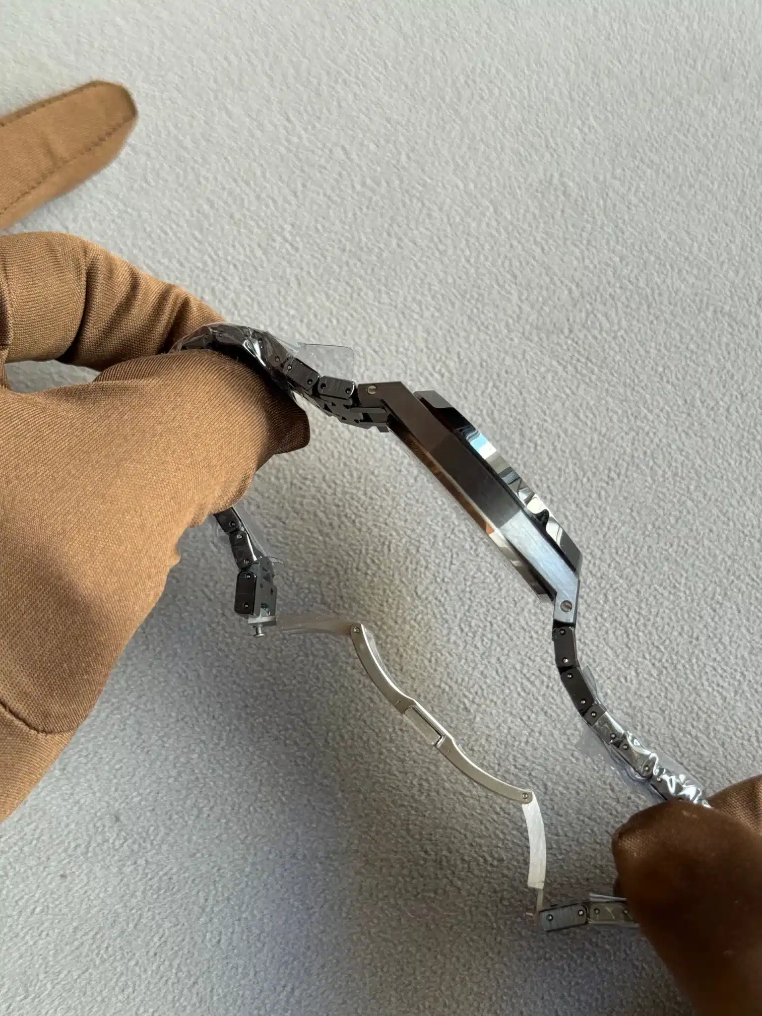 Close-up of a person in a brown sleeve manipulating a small black metal articulated robotic arm on a gray carpet.