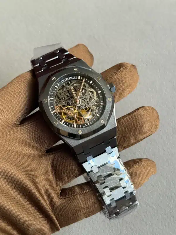 Skeleton Audemars Piguet watch with exposed gears held by a gloved hand on a gray backdrop, shows intricate inner mechanism and metallic strap