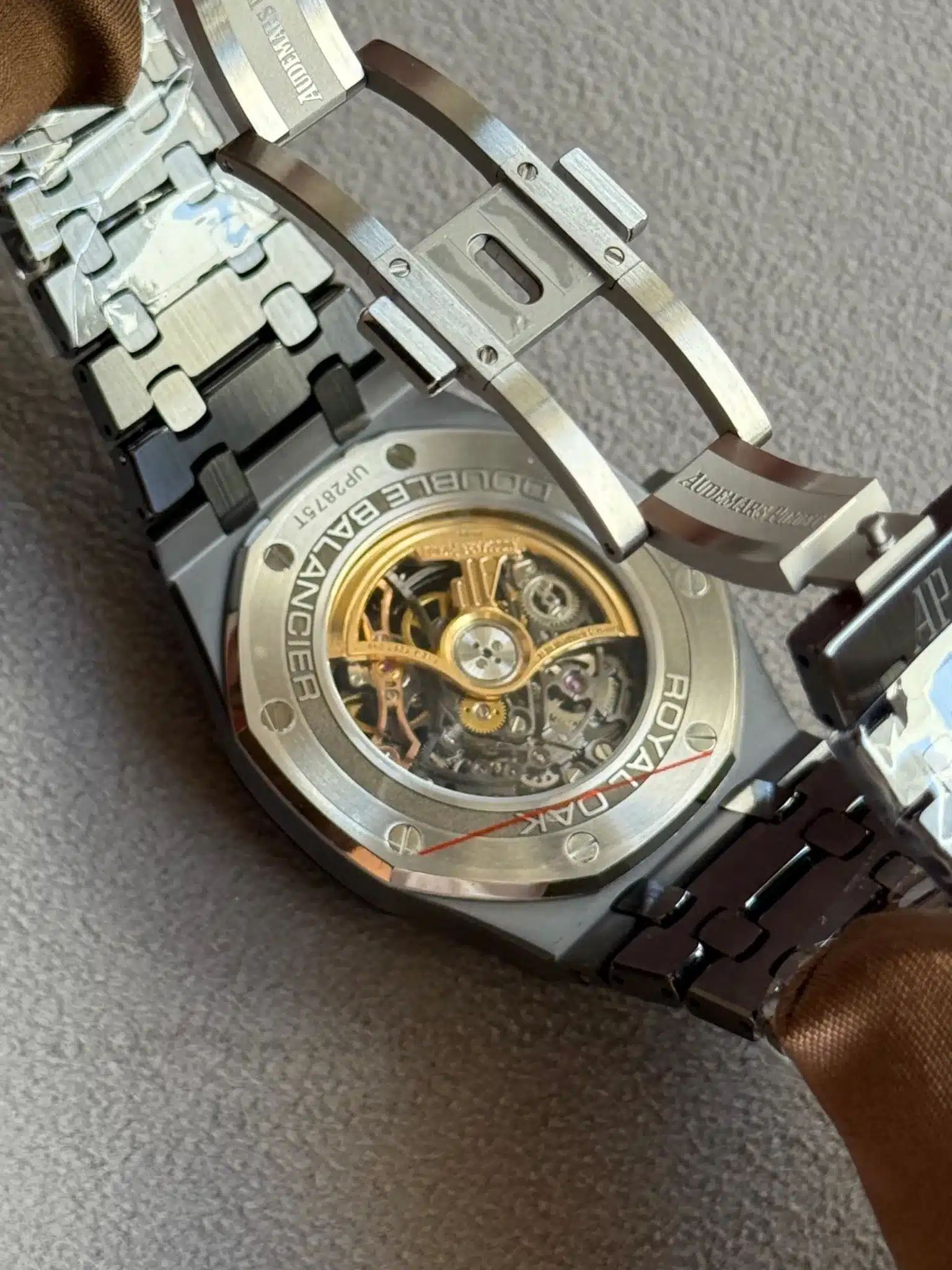 Stainless steel wristwatch with a transparent caseback showing gold-toned rotor and inner gears, Royal Oak branding around the bezel and visible screws in the back plate.