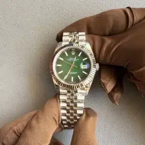 Rolex Datejust watch with a green dial and stainless steel bracelet held by brown-gloved hands against a gray textured background.