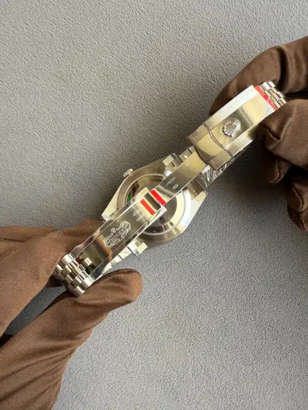 Close-up of a stainless steel Rolex watch held by gloved hands against a gray textured surface.