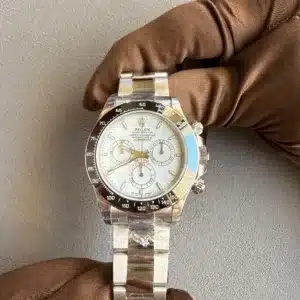 Rolex chronograph watch with white dial and black tachymeter bezel held by a brown-gloved hand against a gray background.