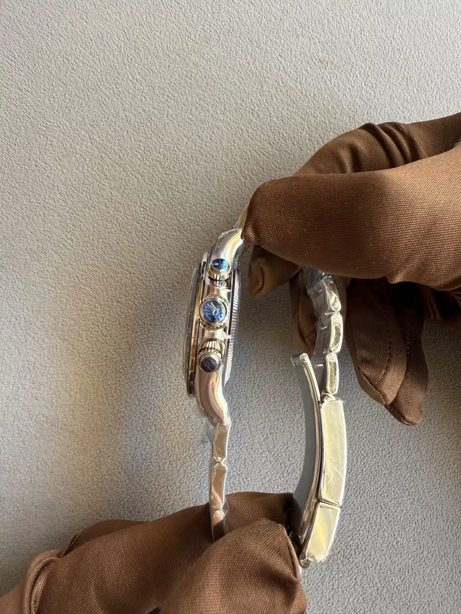 Close-up of a silver bracelet with blue stones resting on a brown fabric sleeve against a textured gray background.