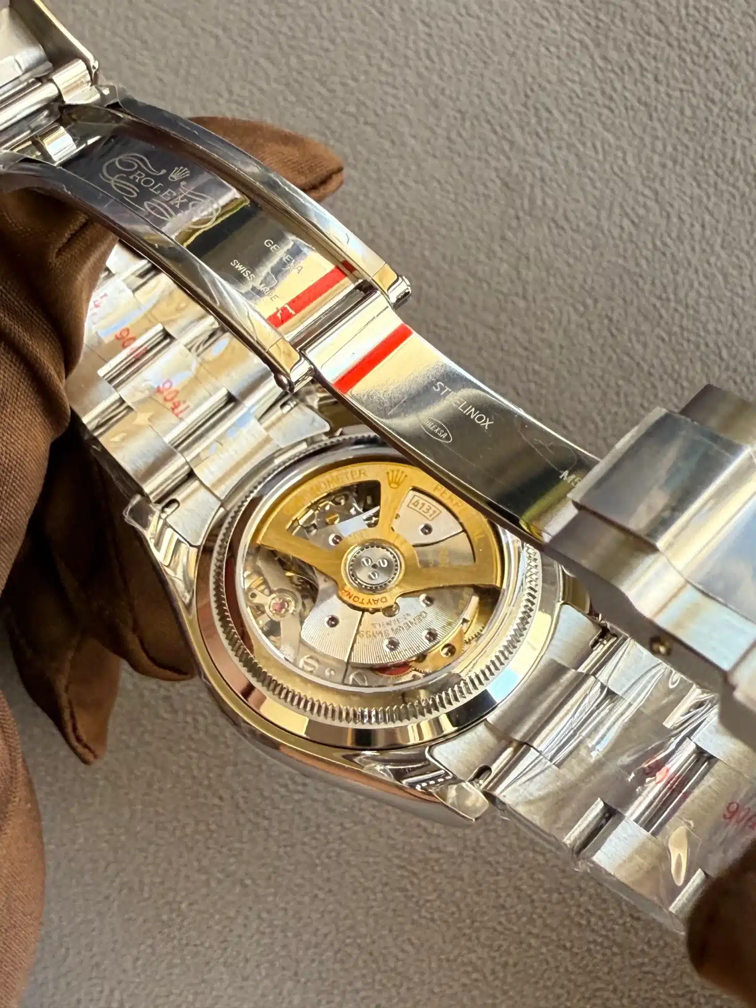 Close-up of a silver Rolex watch showing the inner mechanical movement with a gold rotor and engraved Rolex branding.