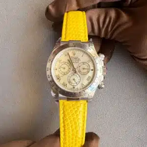Close-up of a Rolex chronograph with a bright yellow textured strap held by gloved hands.