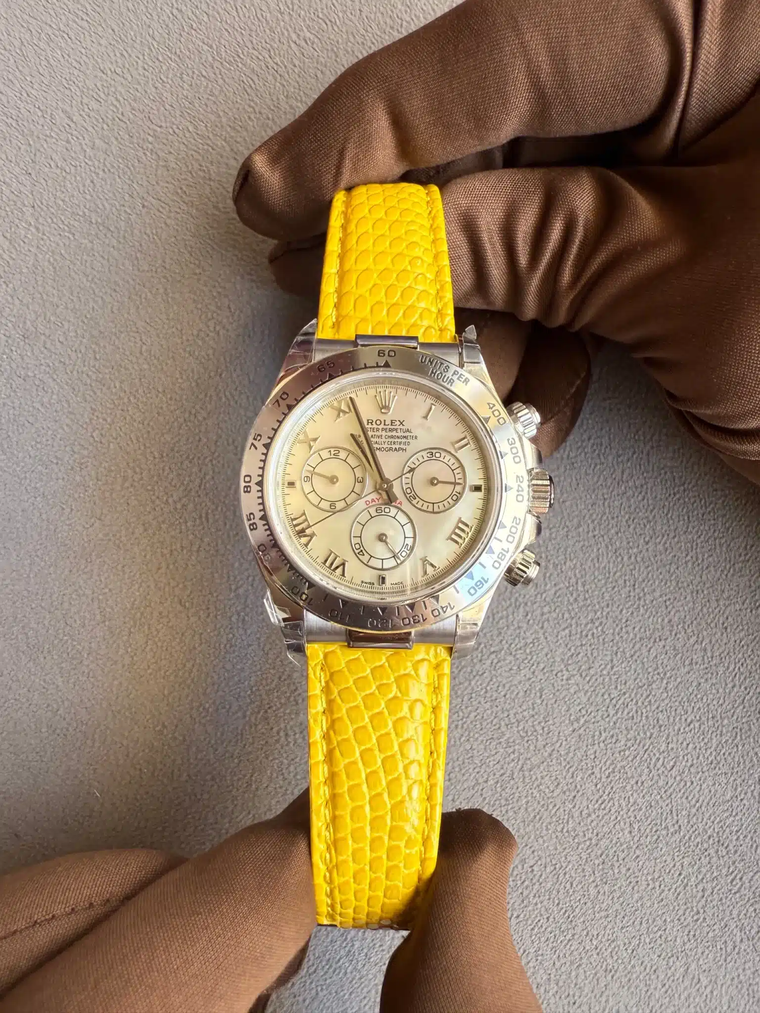 Rolex watch with a bright yellow embossed strap being held by gloved hands on a gray background.