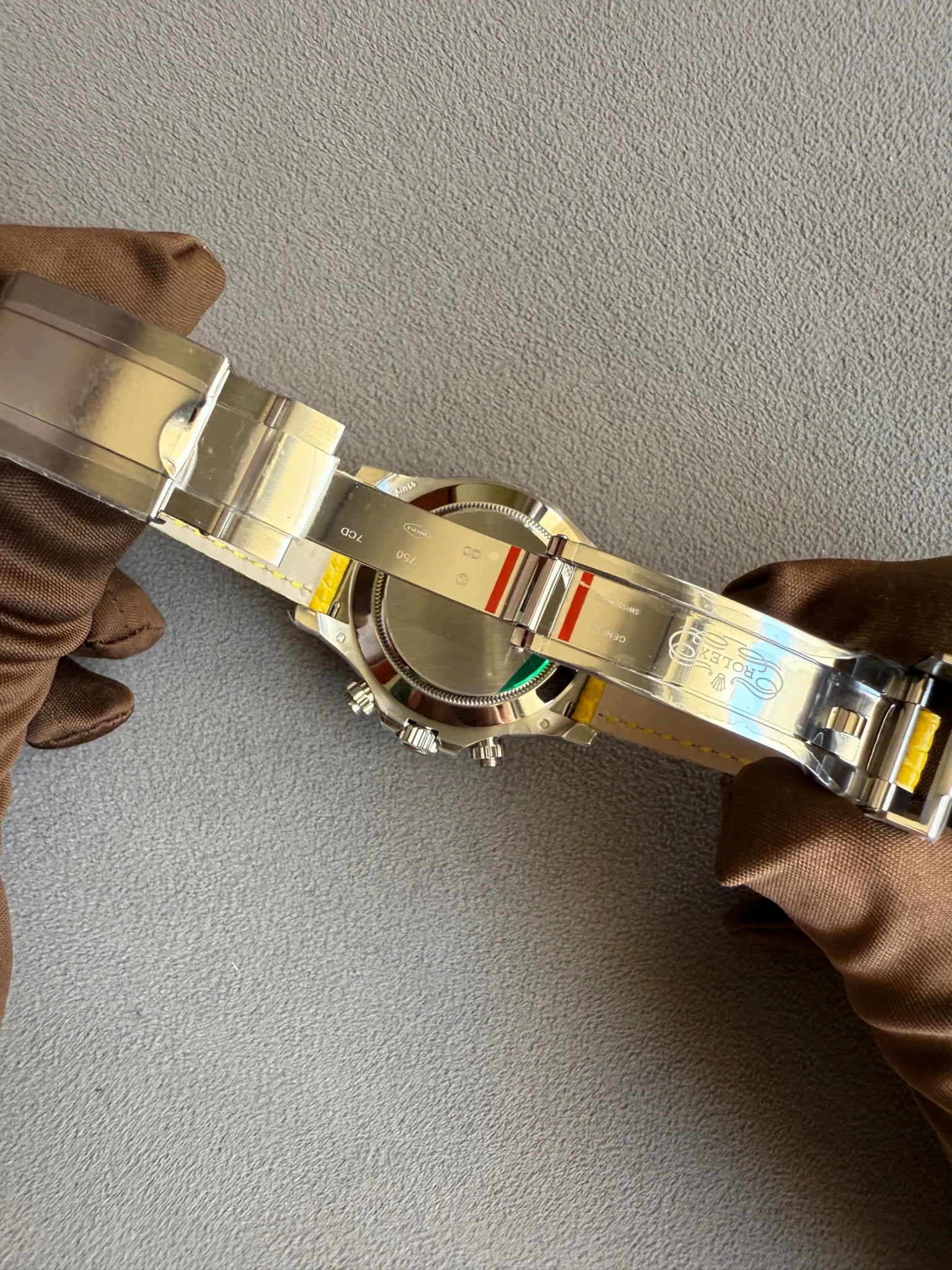 Close-up of a stainless steel wristwatch with a metal bracelet held by brown gloves, showing the case back and crown.