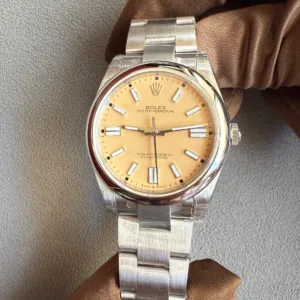 Rolex Oyster Perpetual watch with a tan dial and stainless steel bracelet held by gloved hand on a textured surface