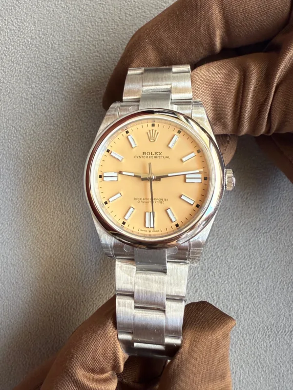 Rolex Oyster Perpetual watch with a tan dial and stainless steel bracelet held by gloved hand on a textured surface