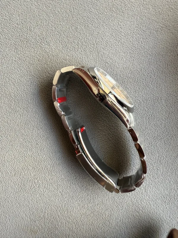 Silver metal wristwatch laid on its side on a gray fabric surface, showing the band and case edges