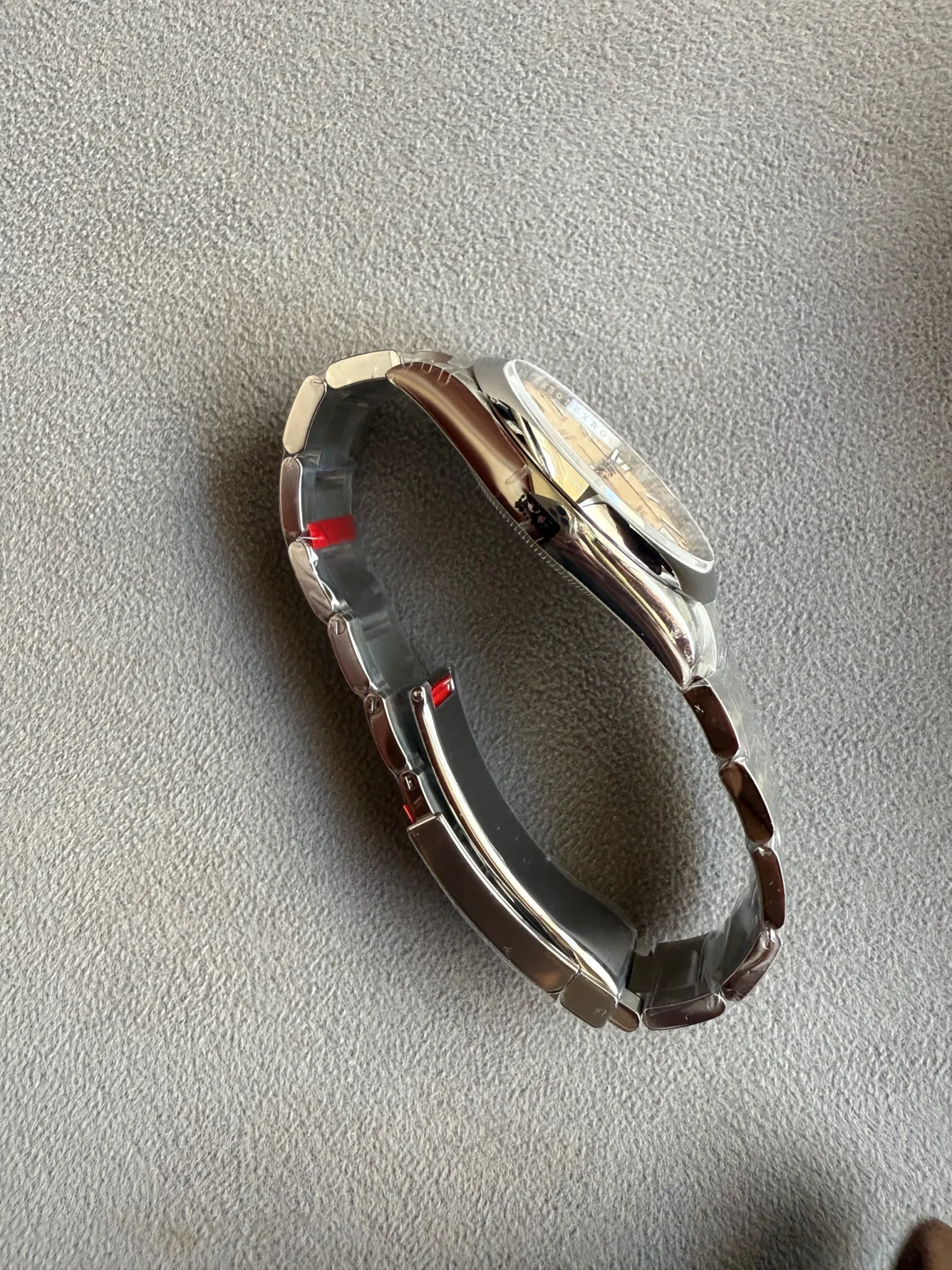 Silver metal wristwatch laid on its side on a gray fabric surface, showing the band and case edges