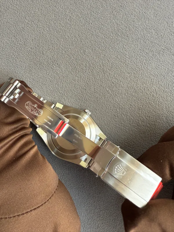 Close-up of a stainless steel Rolex watch on a brown sleeve, resting on a gray carpeted floor.