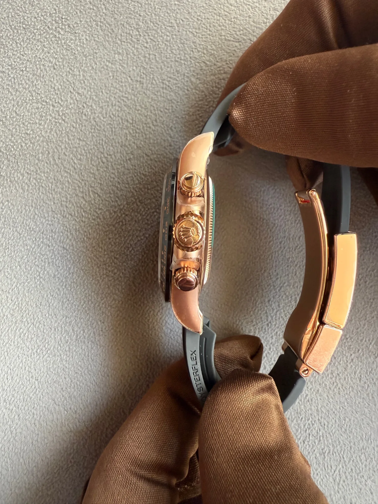 Close-up of a rose-gold wristwatch with a textured crown and side buttons resting on brown fabric background.