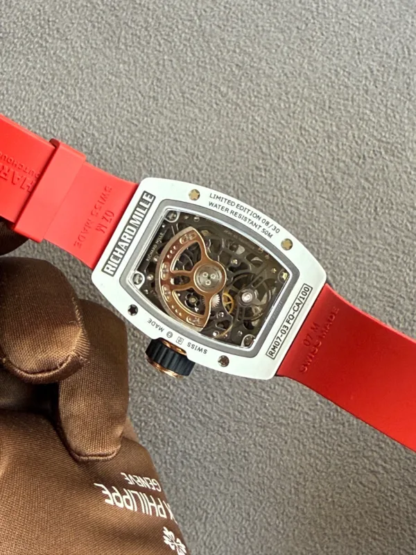 Close-up of a luxury skeleton watch with a bright red strap on a gray carpeted surface.