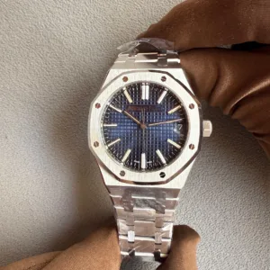 Stainless steel wristwatch with a blue grid dial held by a brown-gloved hand, showing an octagonal bezel with screws and a metal bracelet.