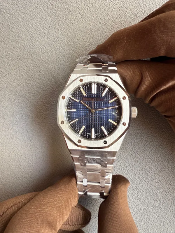Stainless steel wristwatch with a blue grid dial held by a brown-gloved hand, showing an octagonal bezel with screws and a metal bracelet.