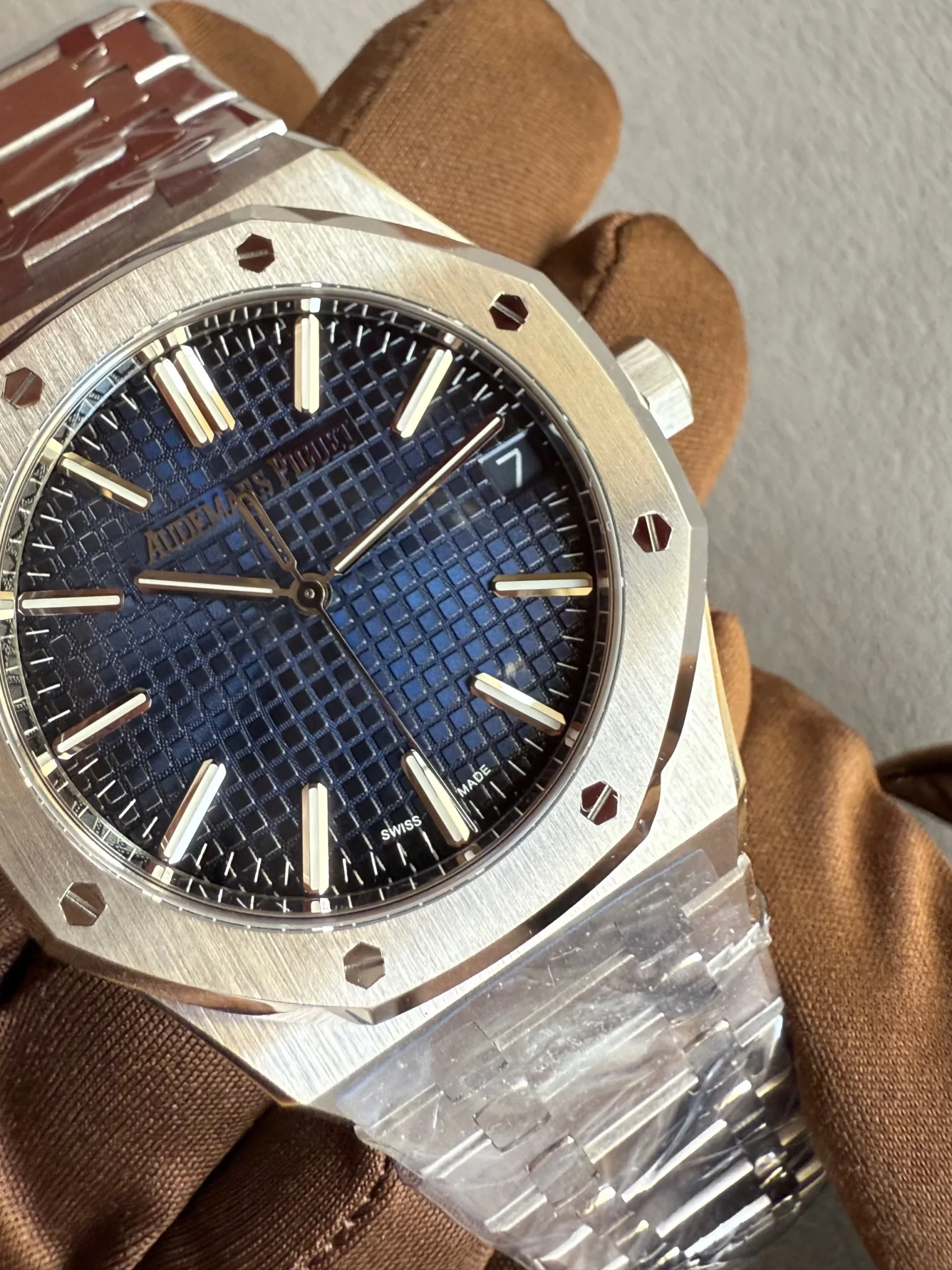 Close-up of an Audemars Piguet luxury watch with a blue patterned dial, baton hour markers, and brushed stainless-steel bezel with hex screws.