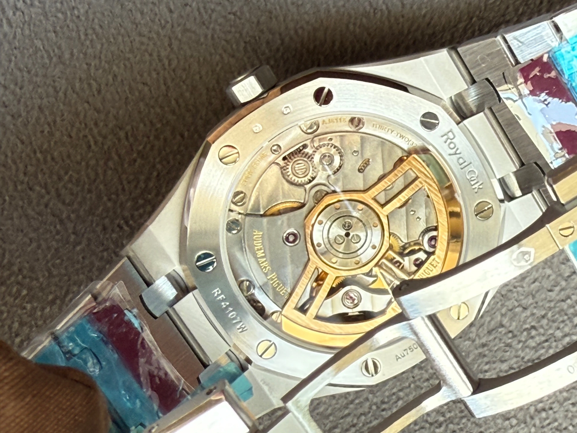 Back of a stainless steel watch with a transparent case showing the intricate mechanical movement and gold rotor inside.