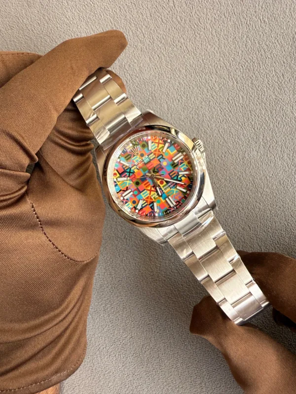 Gloved hand holding a silver metal wristwatch with a colorful patterned dial against a gray background.