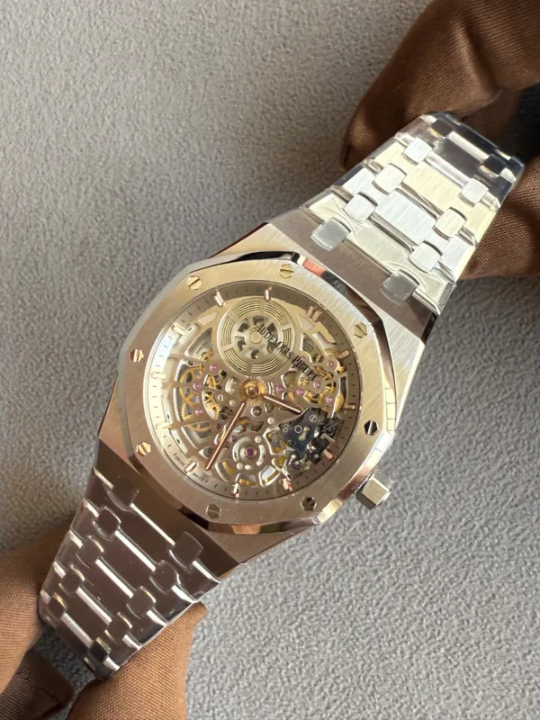 Close-up of a skeleton-dial luxury watch with a silver metal bracelet on a brown glove, showing exposed gears and screws on the bezel.