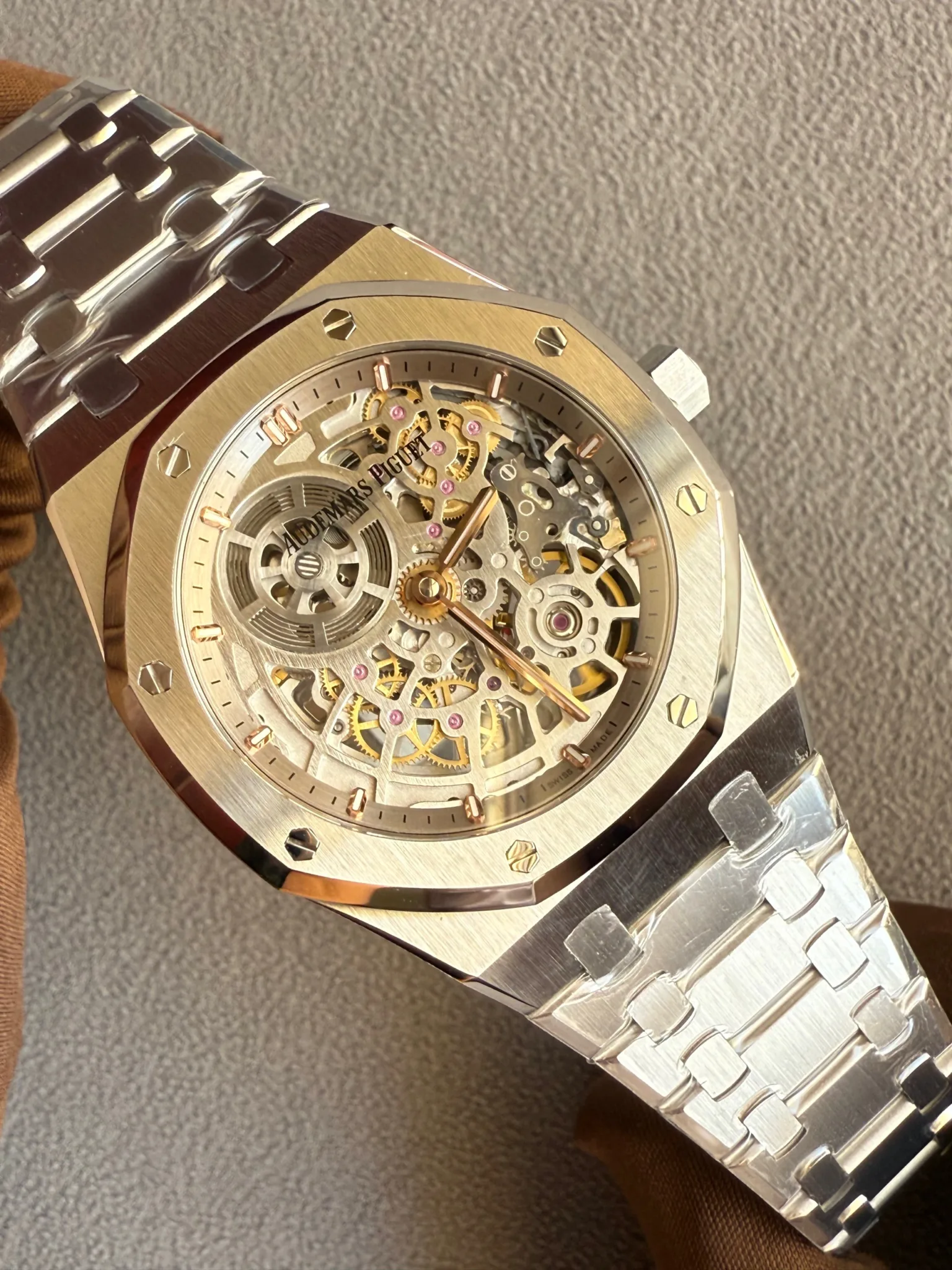 Skeleton wristwatch with exposed gold gears inside a brushed gold case and octagonal bezel with screws; Audemars Piguet logo visible on the movement edge.