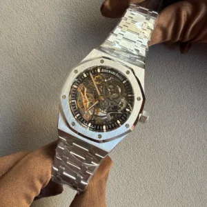Close-up of a skeletonized Audemars Piguet watch with a brushed metal bracelet on a brown-gloved wrist.