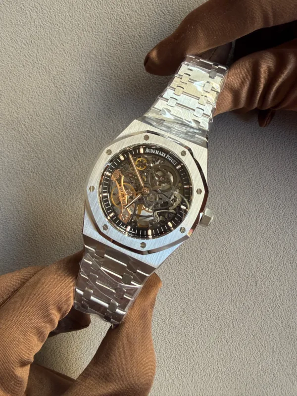 Close-up of a skeletonized Audemars Piguet watch with a brushed metal bracelet on a brown-gloved wrist.