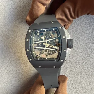 Close-up of a skeleton-dial Richard Mille wristwatch with visible gears and screws, on a dark strap, resting on brown fabric.