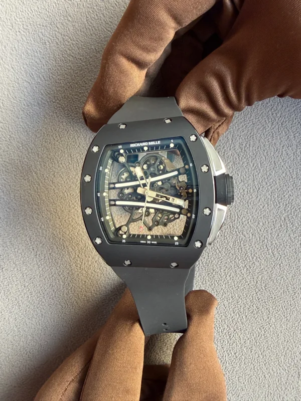 Close-up of a skeleton-dial Richard Mille wristwatch with visible gears and screws, on a dark strap, resting on brown fabric.
