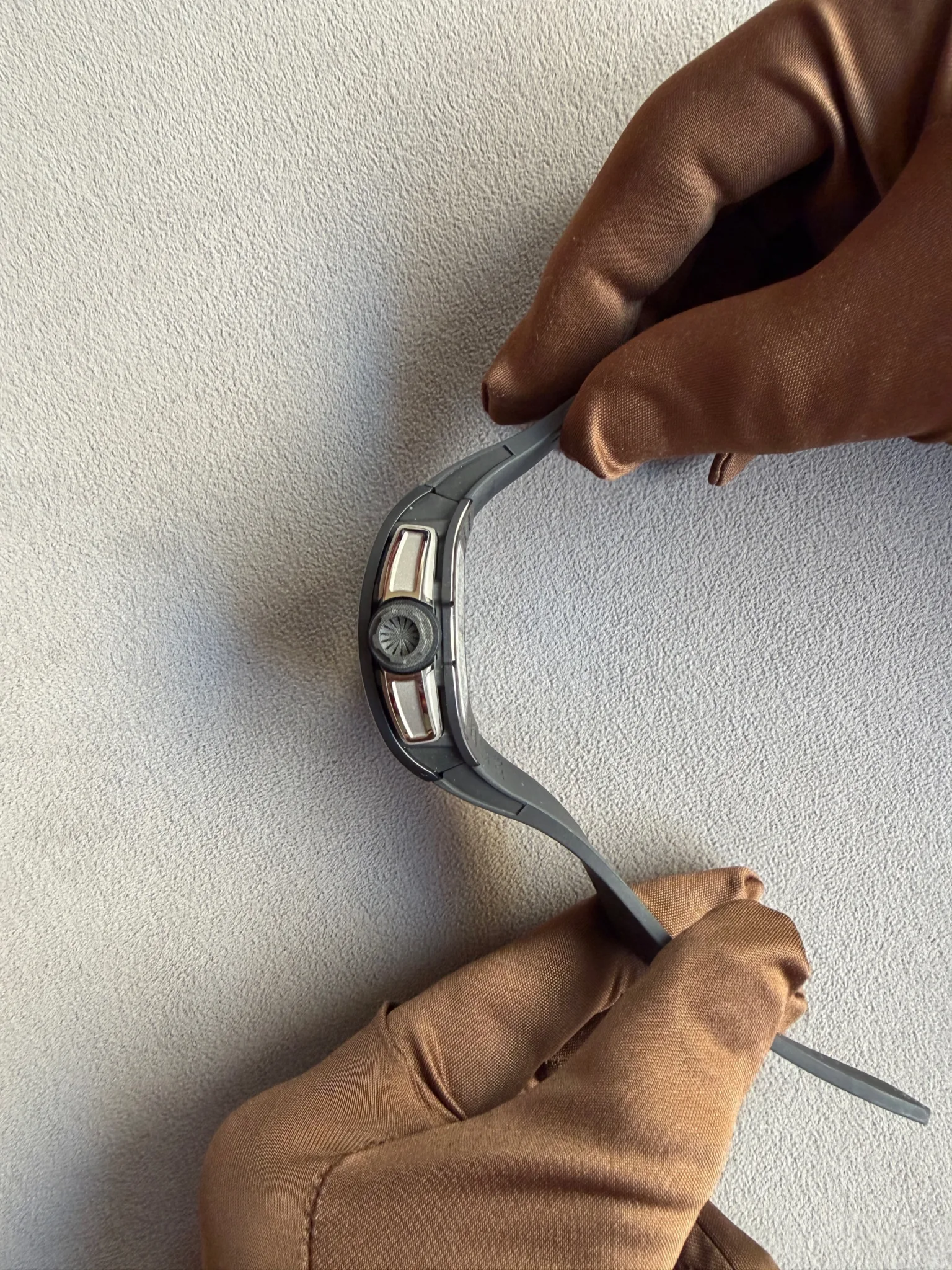 Close-up of gloved hands adjusting a gray smartwatch on a light textured surface.