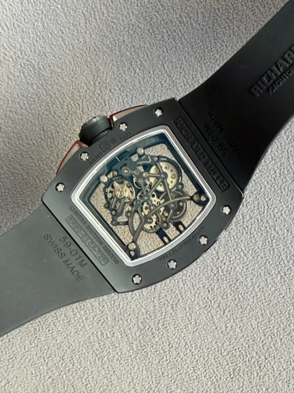 Skeleton-dial wristwatch with visible gears in a square metal case and a black strap on a gray fabric surface