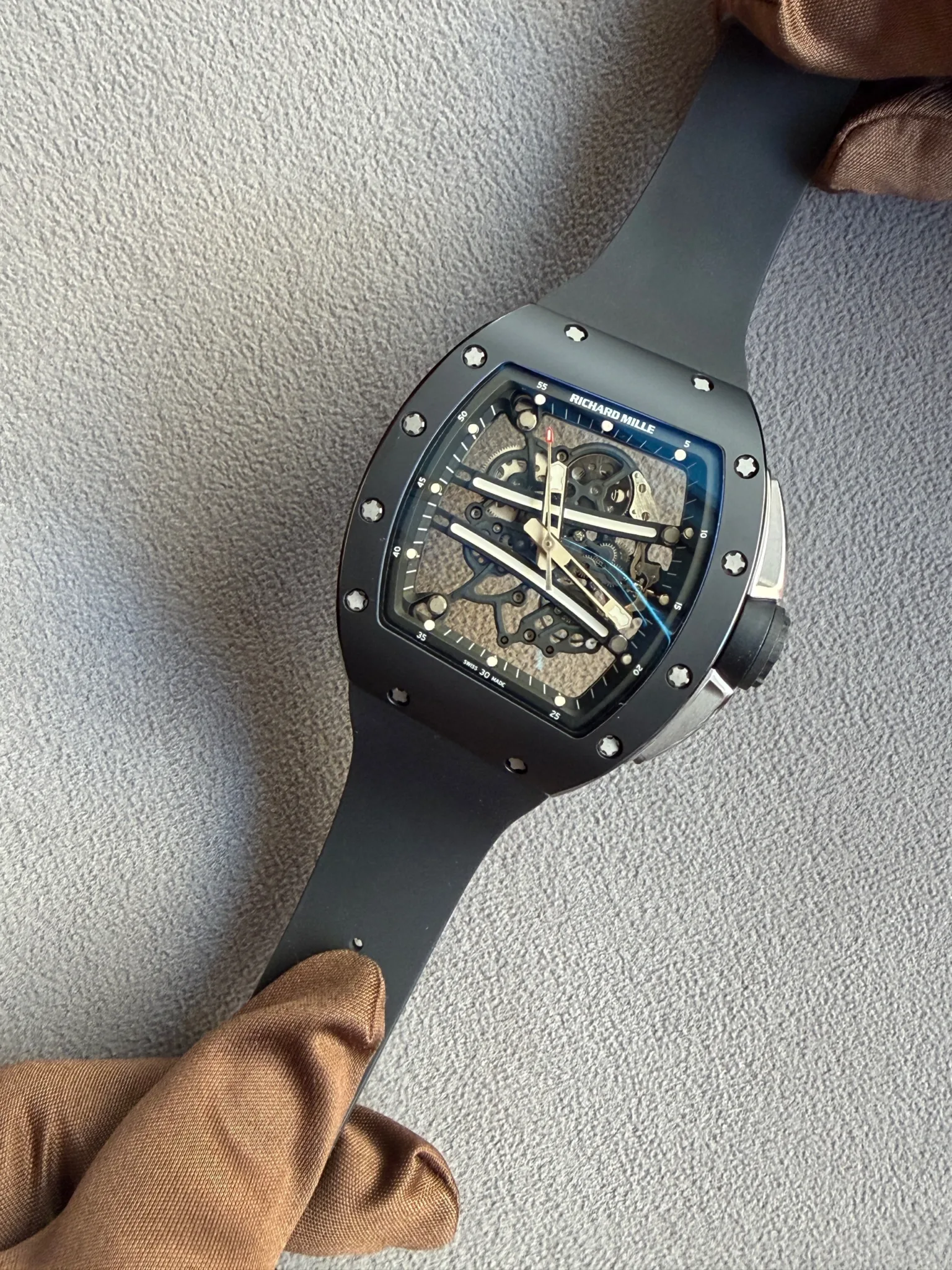 Richard Mille skeleton wristwatch with a black case and visible gears, resting on gray fabric.