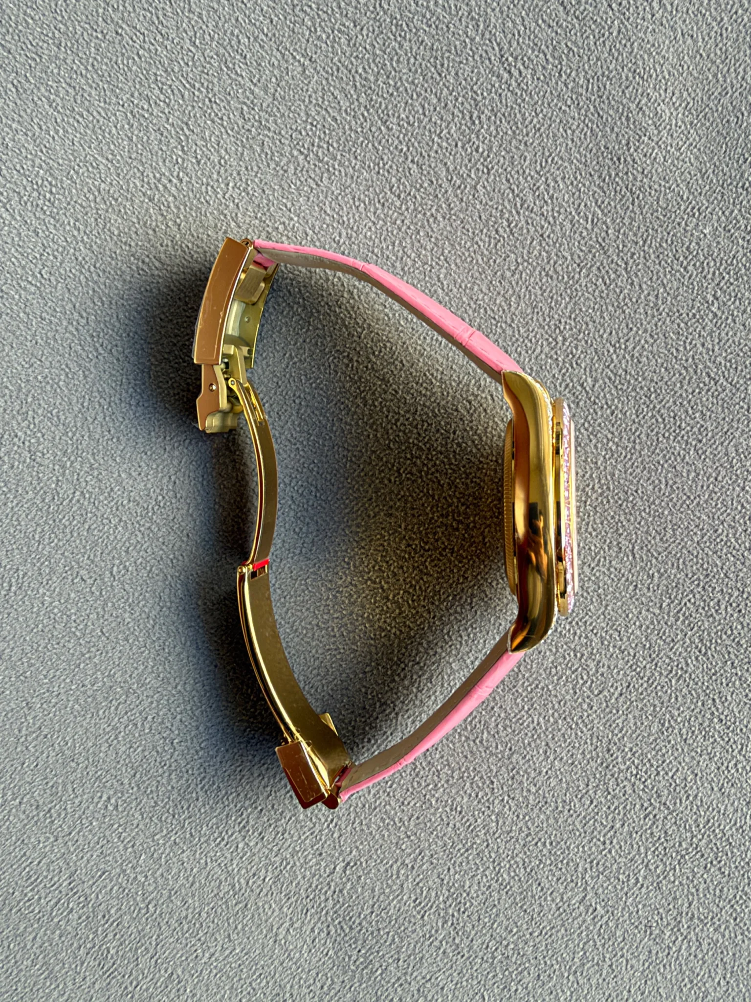 Side view of gold-tone over-ear headphones with a pink headband resting on a gray textured surface