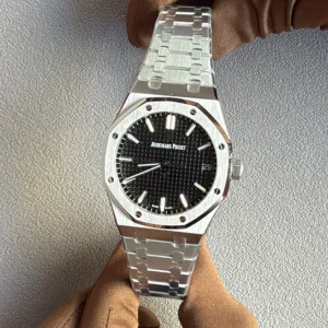 A stainless steel Audemars Piguet Royal Oak wristwatch on a metal bracelet, worn on a gloved hand, with a black textured dial and date window at 3 o'clock.